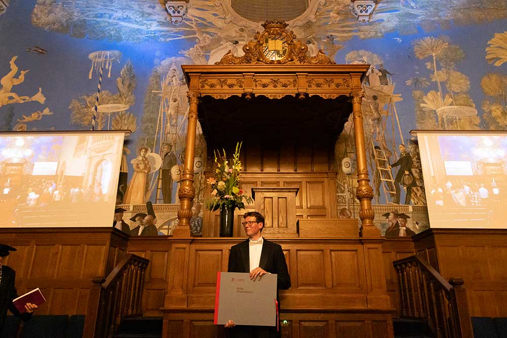 Foto gemaakt teidens een PhD Promotie in de aula de Rijksuniversiteit van Groningen. De promovendus staat met de bull in zijn handen.