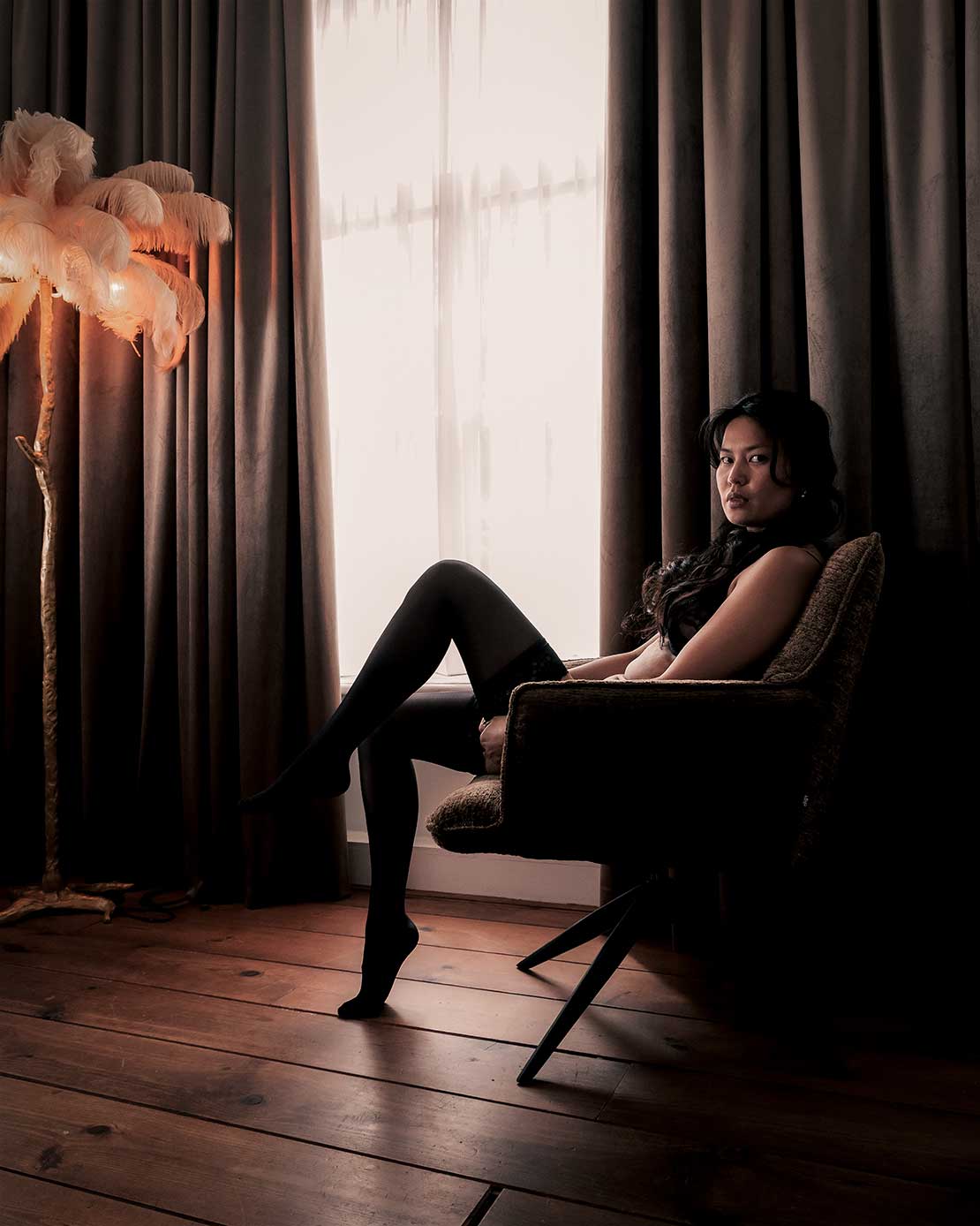 Sfeervolle boudoirfoto van een vrouw zittend op een stoel in een stijlvolle slaapkamer.
