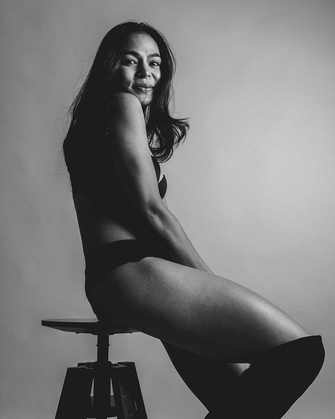 Zwart-wit boudoirfoto van een vrouw in lingerie zittend op een kruk in de studio.