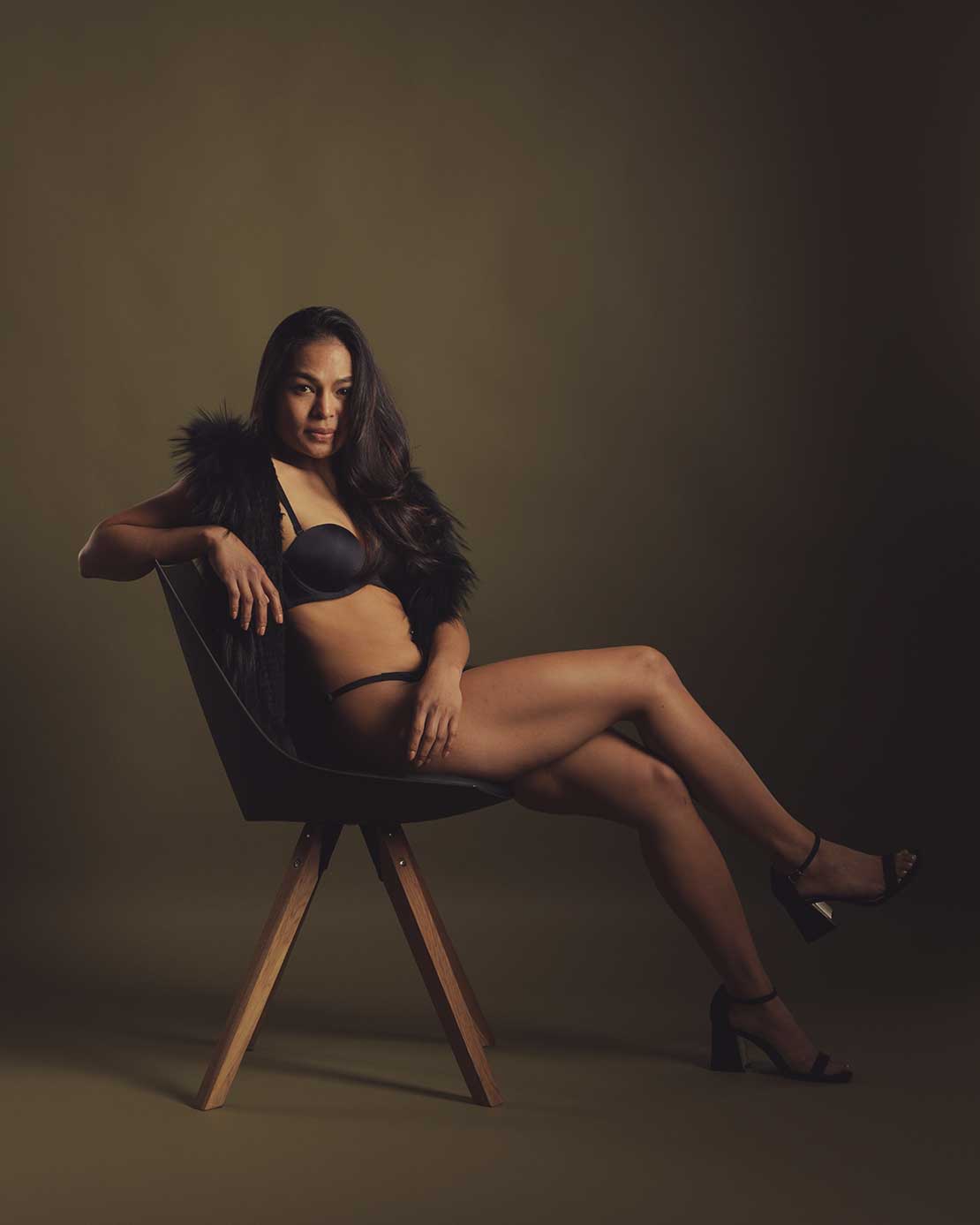 Boudoirfoto van een vrouw in lingerie zittend op een stoel in de studio.