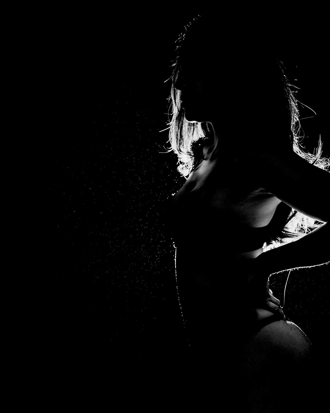 Artistieke zwart-wit boudoirfoto van een vrouw in silhouet met dramatische belichting.