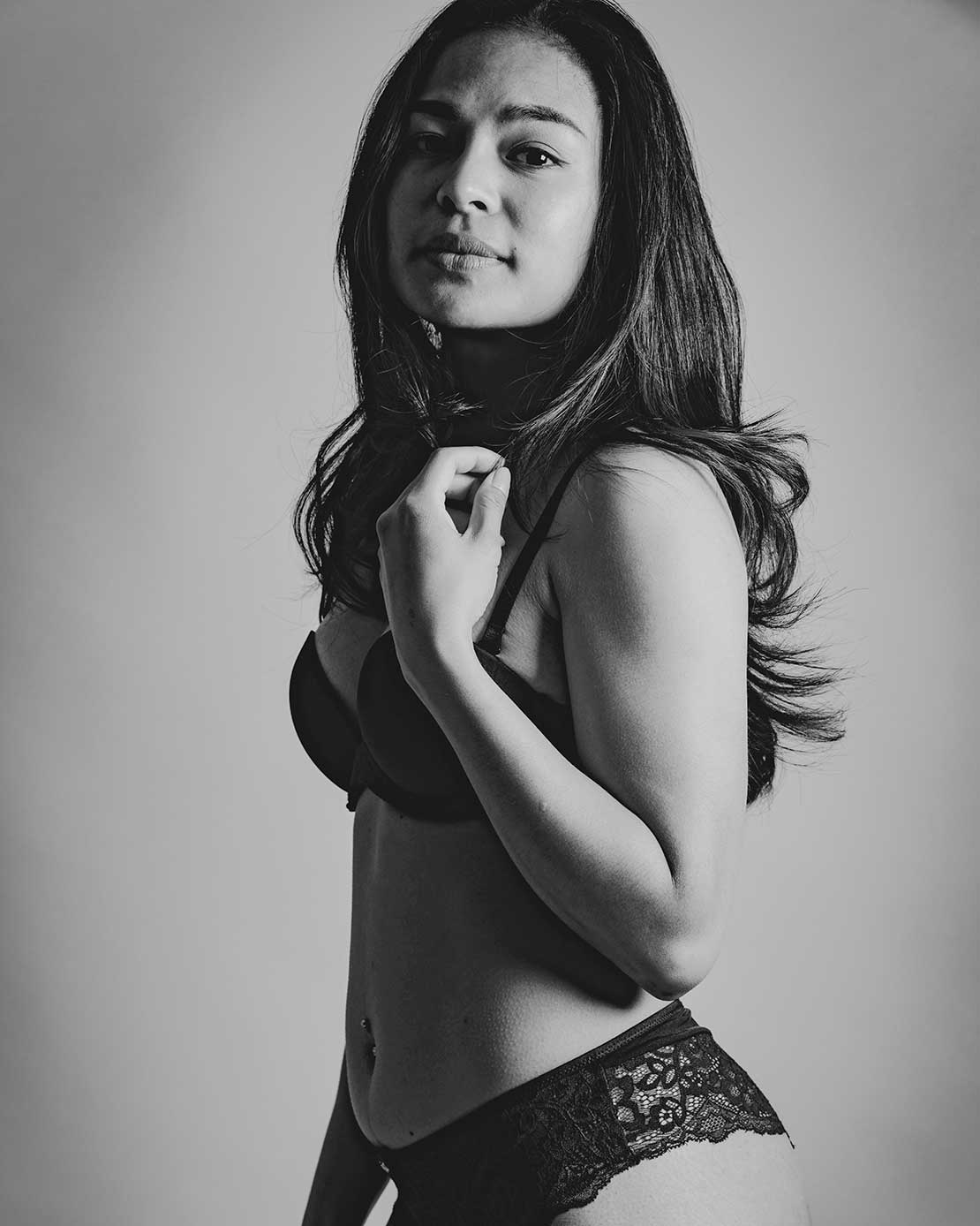 Zwart-wit boudoirfoto van een vrouw in lingerie, elegant geposeerd in de studio.