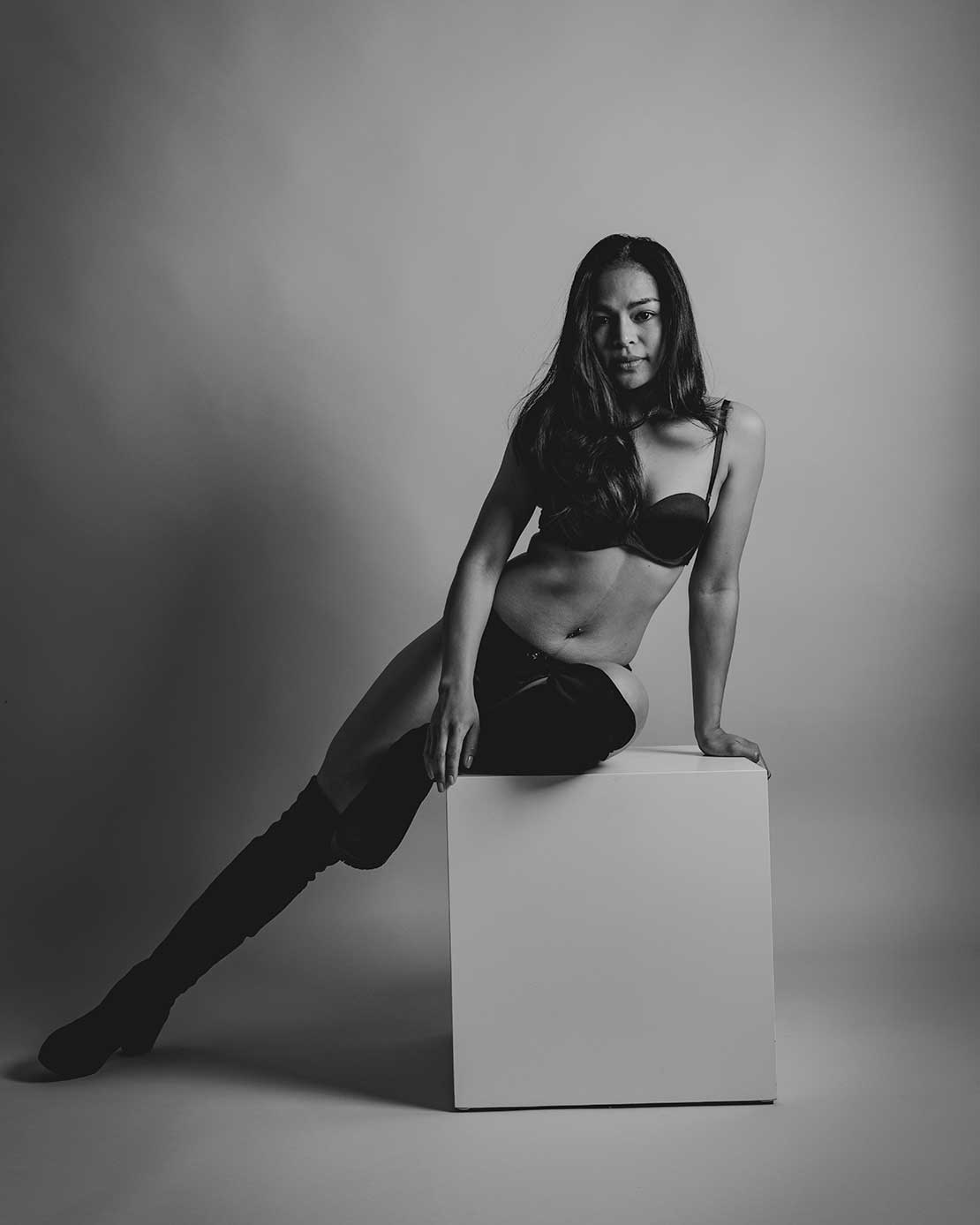 Zwart-wit boudoirfoto van een vrouw in lingerie zittend op een blok in de studio.